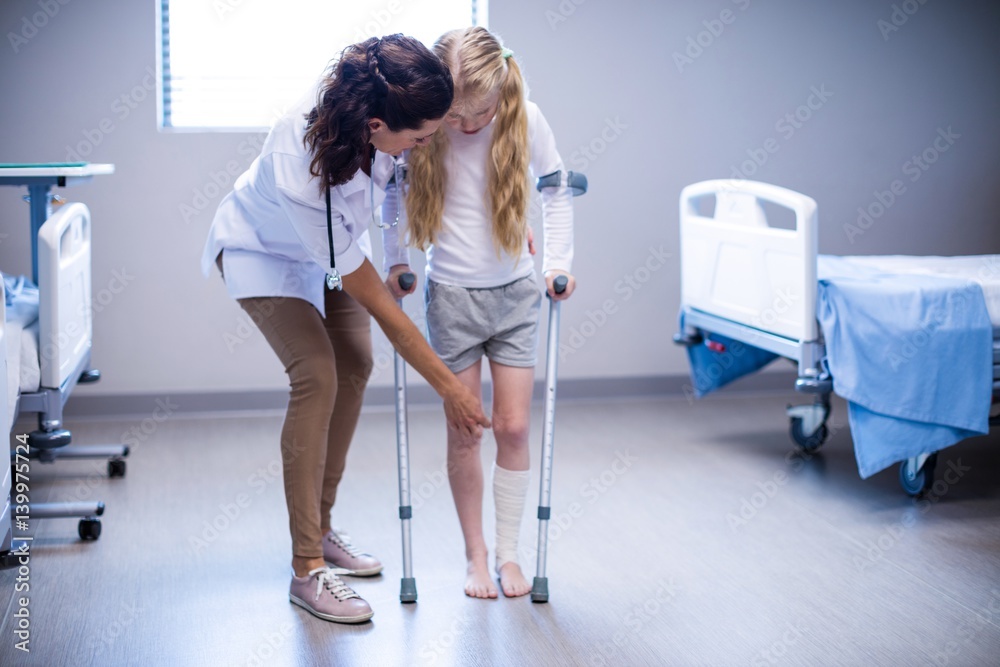 Poster Female doctor assisting girl to walk with crutches in ward