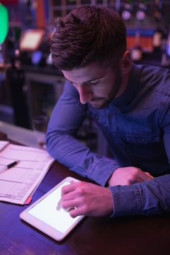 Bartender using digital tablet at bar counter