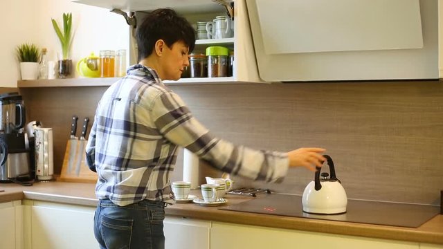 Woman boils the water and making coffee while standing in the kitchen
