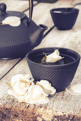 Black cast iron teapot and cup with rose on old wooden table. Tea with roses.