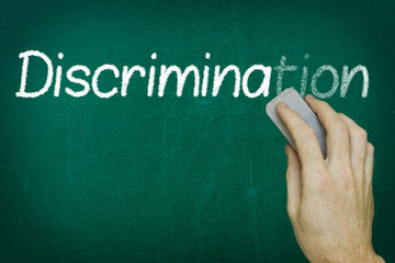 Hand erasing the word DISCRIMINATION written on blackboard