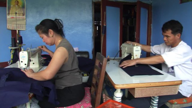 Thailand: Pan across garment factory sewing room, workers assembling jeans