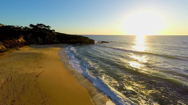 4k Drone flying over sand beach pacific ocean rocks torward sunset