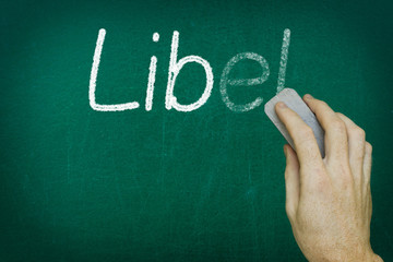 Hand erasing the word LIBEL written on blackboard