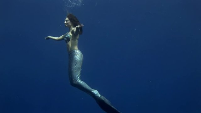 Young girl model underwater mermaid costume on blue background poses in Red Sea. Filming a movie at camera. Extreme sport in marine landscape, coral reefs, ocean inhabitants.