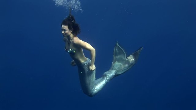Young girl model underwater mermaid costume on blue background poses in Red Sea. Filming a movie at camera. Extreme sport in marine landscape, coral reefs, ocean inhabitants.