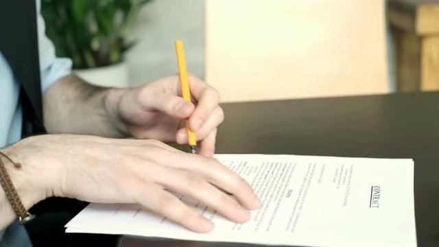 Left-handed businessman sitting by the table signing contract, steadycam shot
