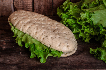Panini with lettuce leaves - italian sandwich on a wooden surface