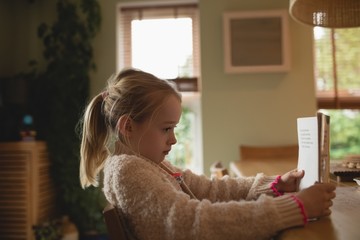 Cute girl sitting at table and reading book