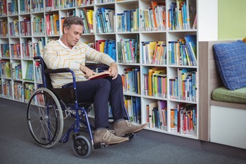 Attentive disabled school teacher reading book in library