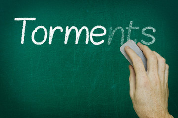 Hand erasing the word TORMENTS written on blackboard
