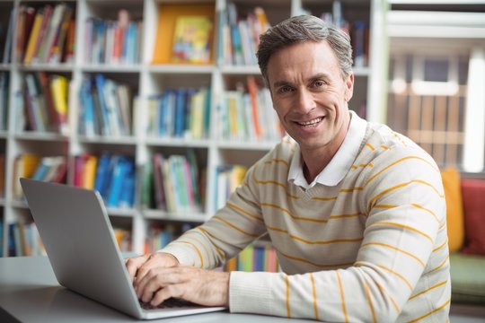 Portrait of happy school teacher using laptop in library