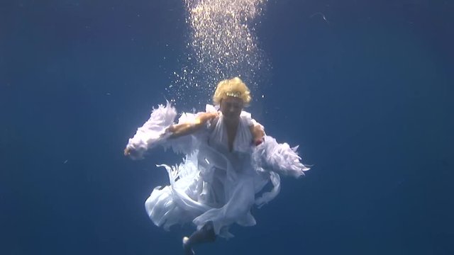Young girl model free diver underwater white angel costume poses in Red Sea. Filming a movie. Extreme sport in marine landscape, coral reefs, ocean inhabitants. Free diver.