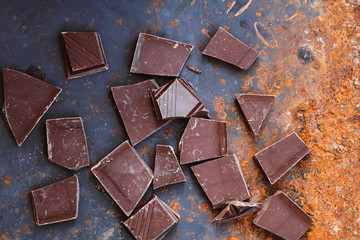 Top view of a rusty vintage baking sheet with crumbled chocolate bars. Dark photography food background.