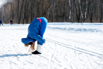 Fototapeta na wymiar Beautiful young girl stretches on a sports field in winter against a background of deciduous forest. Winter sports concept photo