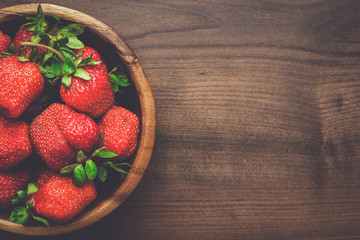 wooden bowl full of fresh strawberries on the brown table