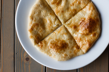 Ossetian pie with potatoes or mutton on a white plate. Wooden background.