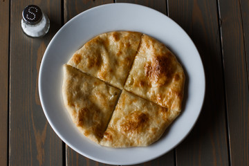 Ossetian pie with potatoes or mutton on a white plate. Wooden background.