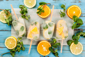Homemade ice cream, frozen mojito cocktail (lemon and mint, mint and orange). Popsicle, on blue rustic table. top view, with fresh mint leaves and slices of fruits