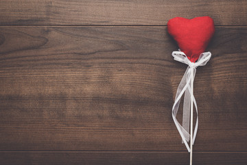red plush heart shape on stick over wooden background