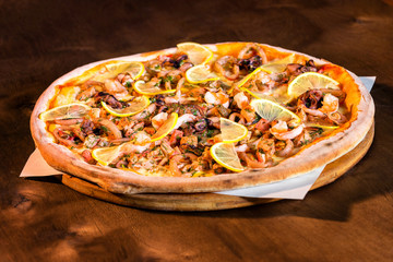 Tasty italian pizza with seafood on wooden tray at table background.