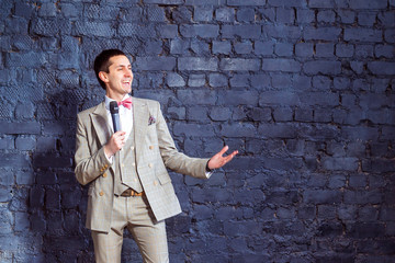 Elegant young man with microphone is pointing at wall background with space for text.