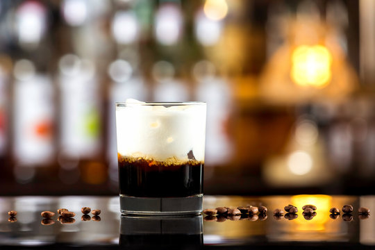 Closeup image of glass of black Russian cocktail and coffee beans at dark bar stand background.