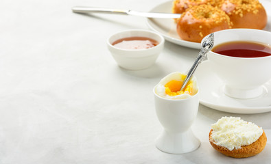 Delicious and healthy breakfast of boiled egg and brioche buns with black tea on a light background. Copy space, soft focus.