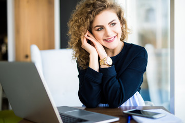Obraz premium Young attractive woman at a modern office desk, working with laptop, looking at the window, thinking about a post.