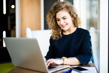 Happy curlu young woman use laptop in modern place with bright windows.