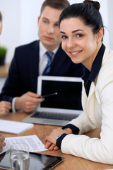 Group of business people and lawyers discussing contract papers sitting at the table. Focus at brunette woman looking at camera