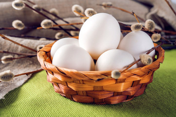 Eggs in a wicker basket on a green fabric background and a pussy-willow branch. Linen rustic fabric background