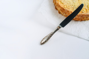Delicate light cake on a white paper on a table on a light background, selective focus. From above. A layered piece of cake, next to it is a metal vintage knife. There is free space for text.