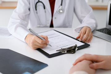 Fototapeta premium Close up of a female doctor filling up an application form while consulting patient. Medicine and health care concept