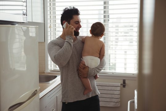 Father talking on mobile phone while holding his baby