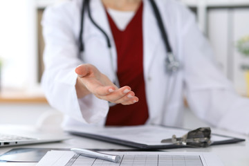 Fototapeta premium Close up of unknown female doctor typing on laptop computer while sitting at the table. Medical staff, compulsory work concept
