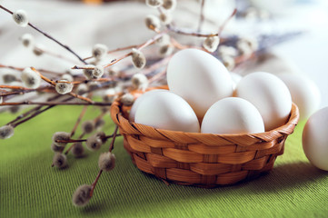 Eggs in a wicker basket on a green fabric background and a willow branch