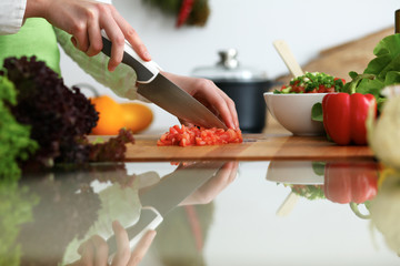 Close-up of human hands cooking vegetables salad in kitchen on the glass table with reflection. Healthy meal and vegetarian concept