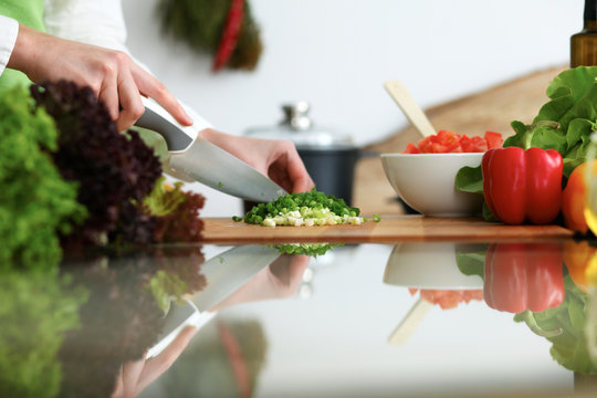 Close-up of human hands cooking vegetables salad in kitchen on the glass table with reflection. Healthy meal and vegetarian concept