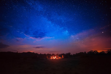 Camping fire under the amazing blue starry sky with a lot of shining stars and clouds. Travel...