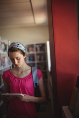 Fototapeta na wymiar Attentive schoolgirl using digital tablet in library