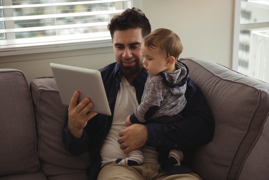 Father using digital tablet while holding his baby