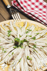 Close-up of anchovies with olive oil and vinegar on a wooden plate next to a fork on a brown wooden table. Healthy food. Vertical shoot