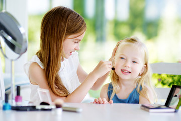 Two cute funny sisters applying make-up on sunny summer day at home