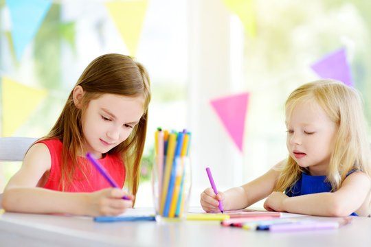 Two cute little sisters drawing with colorful pencils at a daycare. Creative kids painting together.