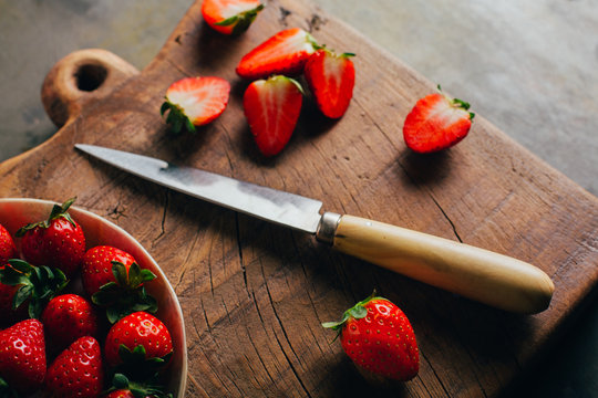 Cutting strawberries on wooden cutting board over grunge background