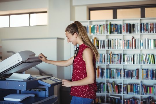 Happy schoolgirl using Xerox photocopier in library