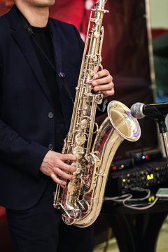 Gold saxophone with specks on it in male hands in the red background.Hands of musician playing alto saxophone, closeup,Hands of groom play on saxophone,jazz music concept