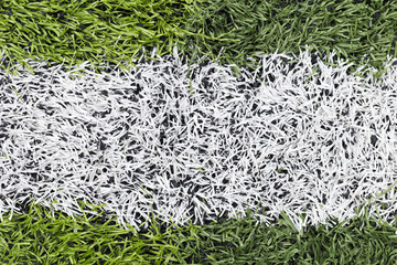 Close-up view of artificial turf with a bright white line, used in sports fields such as football...
