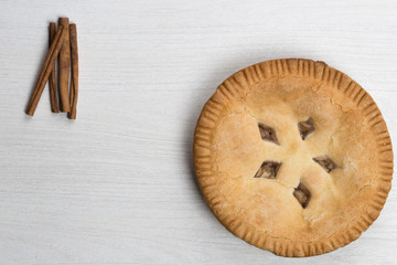 Apple pie cake lying on wooden white background with cinamon sticks